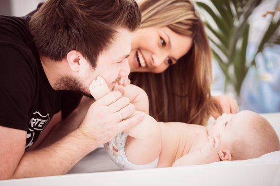 Eltern spielen liebevoll mit ihrem Baby auf einer gemütlichen Unterlage.